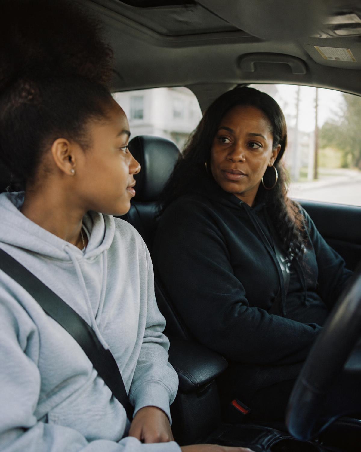 A mother and her teenage daughter talking in a parked car