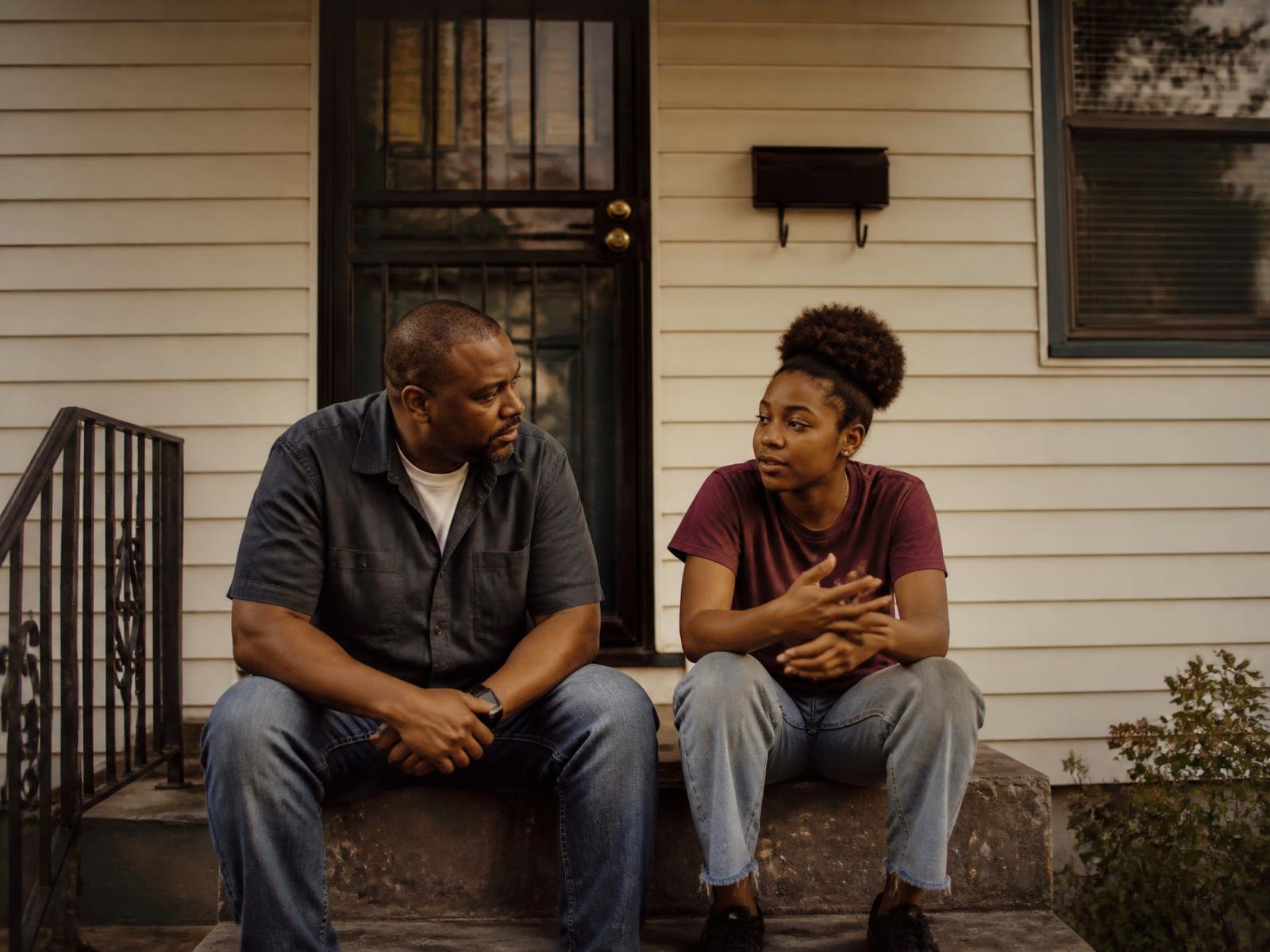 A father and his teenage daughter sitting together on their front steps, mid-conversation