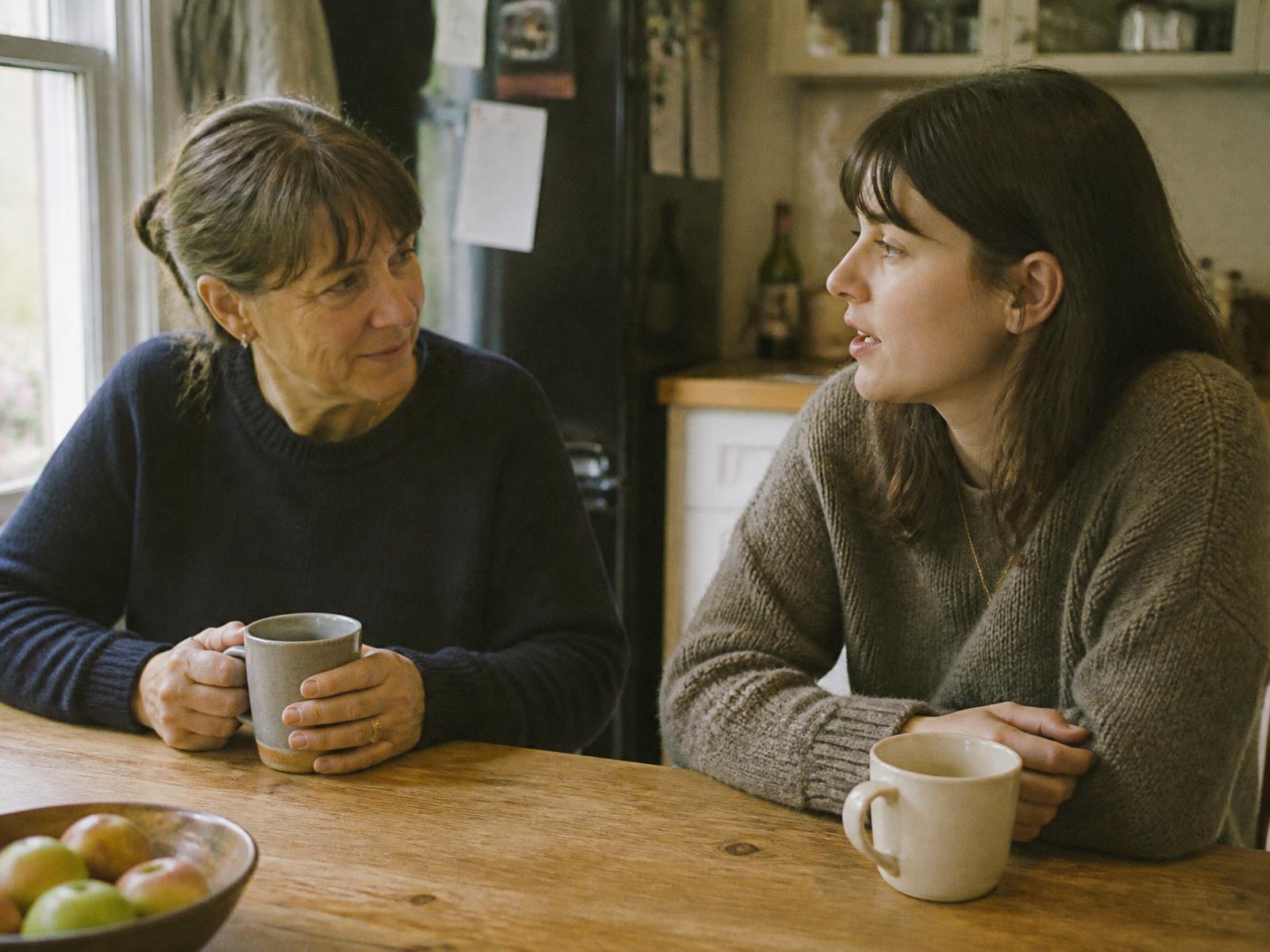 A mother and her grown daughter talking over coffee at a kitchen table