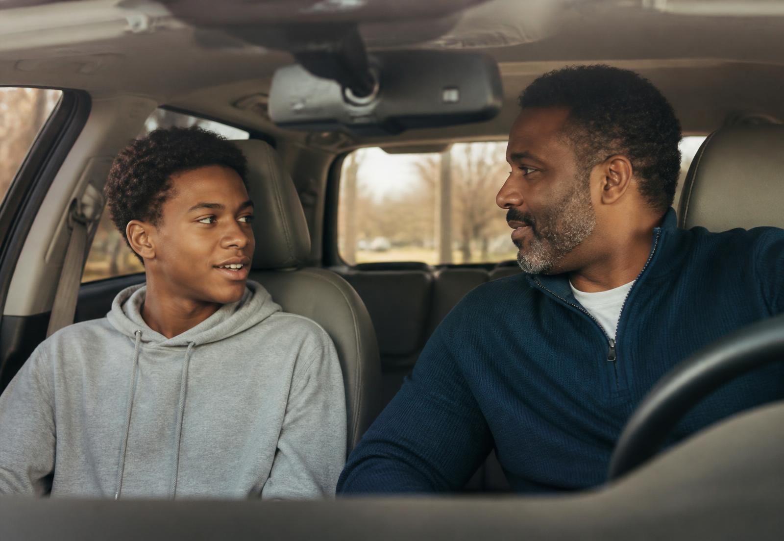A father and his teenage son talking in a parked car